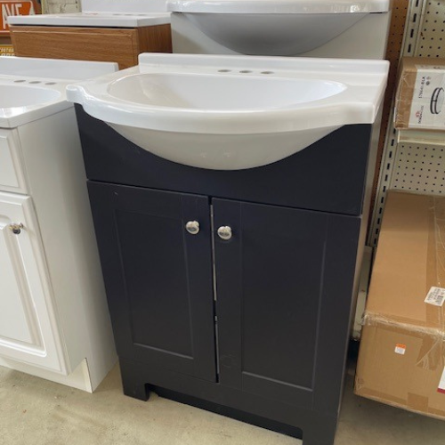 Close-up of our display of vanities, focusing on a black vanity with a white sink and countertop, black cabinets, and silver hardware.