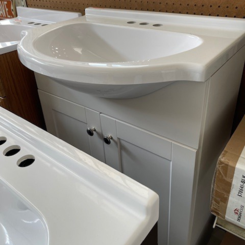 Close-up of our display of vanities, highlighting a white vanity with a white sink and countertop, white cabinets, and silver hardware.