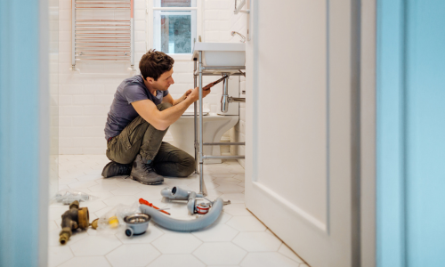 A man kneeling next to a sink, working on the plumbing with a wrench.